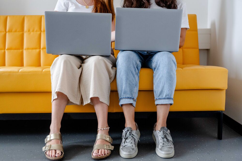 Studierende sitzen mit Laptop auf einer gelben Couch.