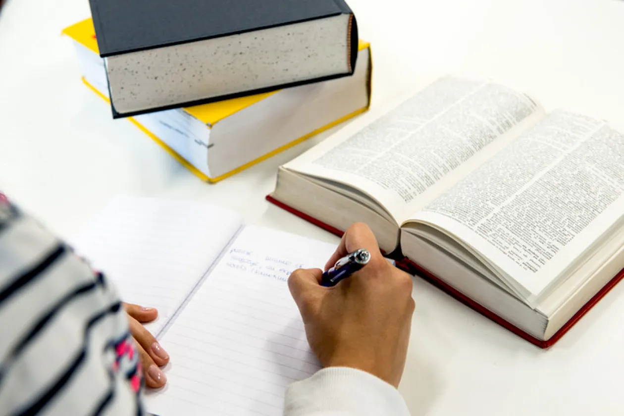 Hand mit Stift und Block mit geöffnetem Buch
