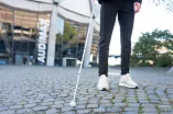 Eine Person tastet mit einem weißen Langstock das Pflaster vor dem Audimax ab 