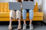 Studierende sitzen mit Laptop auf einer gelben Couch.