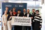 Foto: Einige Personen stehen und gucken lächelnd in die Kamera. Sie halten ein Banner mit dem Logo des Deutschlandsstipendiums auf Bauchhöhe.