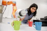 Eine Frau nimmt eine Tasse, in die ein Roboterarm Wasser schüttet