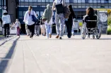 Verschiedene Menschen überqueren die Unibrücke, darunter eine Rollstuhlfahrerin, sie sind von hinten zu sehen