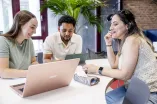 drei Studierende sitzem am Tisch, unterhalten sich und schauen auf Laptops