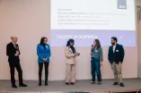 Foto: Fünf Personen stehen nebeneinander auf einer Bühne. Die Person in der Mitte hält Moderationskarten in der Hand.