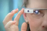 Foto: ein Teoi vom Gesicht einer Jungen Frau, die Smartglasses trägt uind eine Hand an den Sensor hält