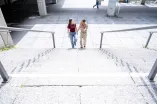 Foto: ZWei Personen, eine männliche und eine weiblich gelesene, steigen ein Treppe hoch und unterhalten sich dabei. Das Bild ist von dem oberen Teil der Treppe aufgenommen.