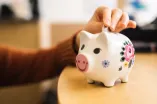 Foto: Sparschwein, in das jemand einen Euro legt.