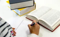 Hand mit Stift und Block mit geöffnetem Buch