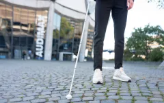 Eine Person tastet mit einem weißen Langstock das Pflaster vor dem Audimax ab 