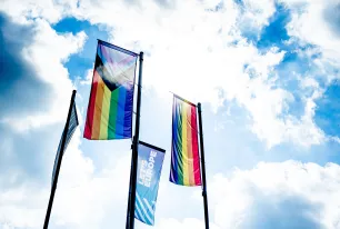 Das Bild zeigt zwei Regenbogenflaggen vor blauem Himmel, außerdem eine Flagge mit dem Logo von "Let´s Europe"