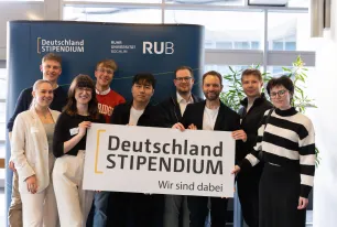 Foto: Einige Personen stehen und gucken lächelnd in die Kamera. Sie halten ein Banner mit dem Logo des Deutschlandsstipendiums auf Bauchhöhe.