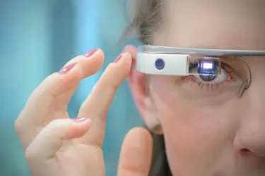 Foto: ein Teoi vom Gesicht einer Jungen Frau, die Smartglasses trägt uind eine Hand an den Sensor hält