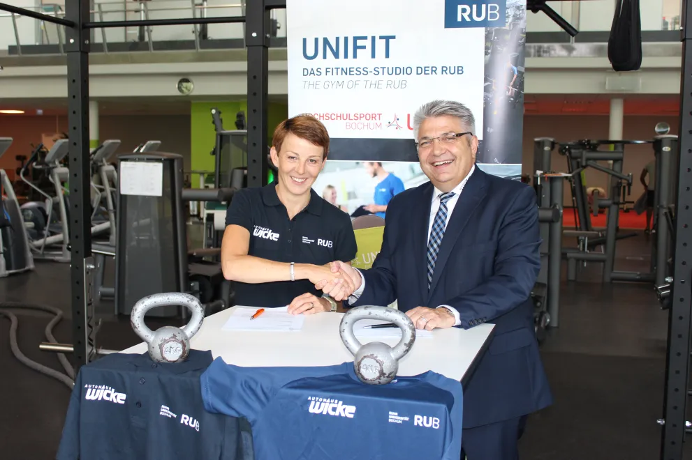 Das Autohaus VW Wicke Bochum und die RUB-Vertreterin des Hochschulsports schütteln sich die Hand und bekräftigen das Sponsoring der Spitzensportler-Austattung.