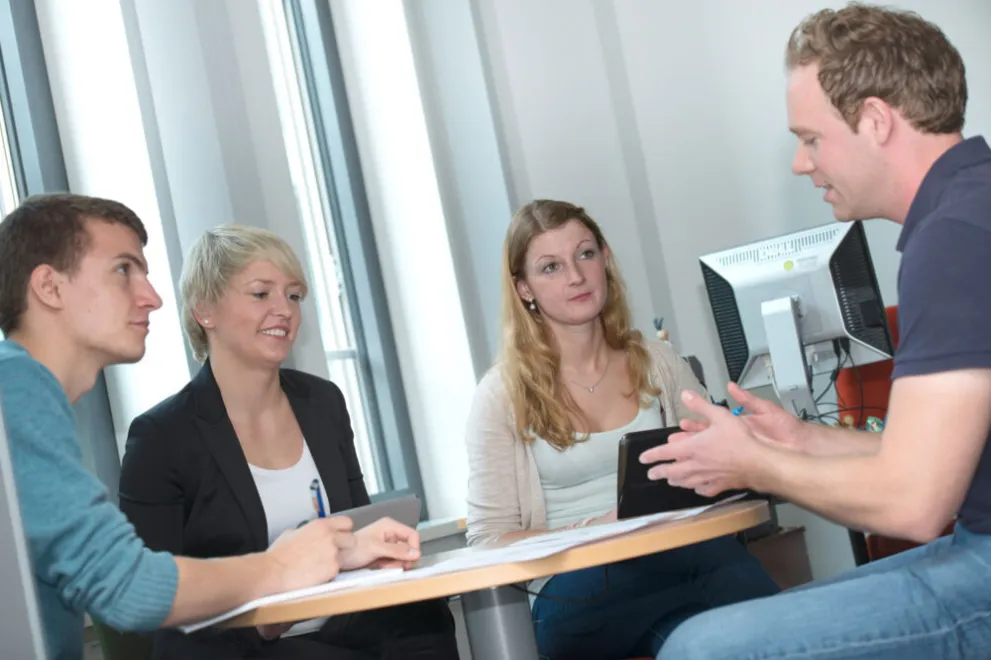 Vier Mitarbeitende sitzen an einem Tisch und unterhalten sich.