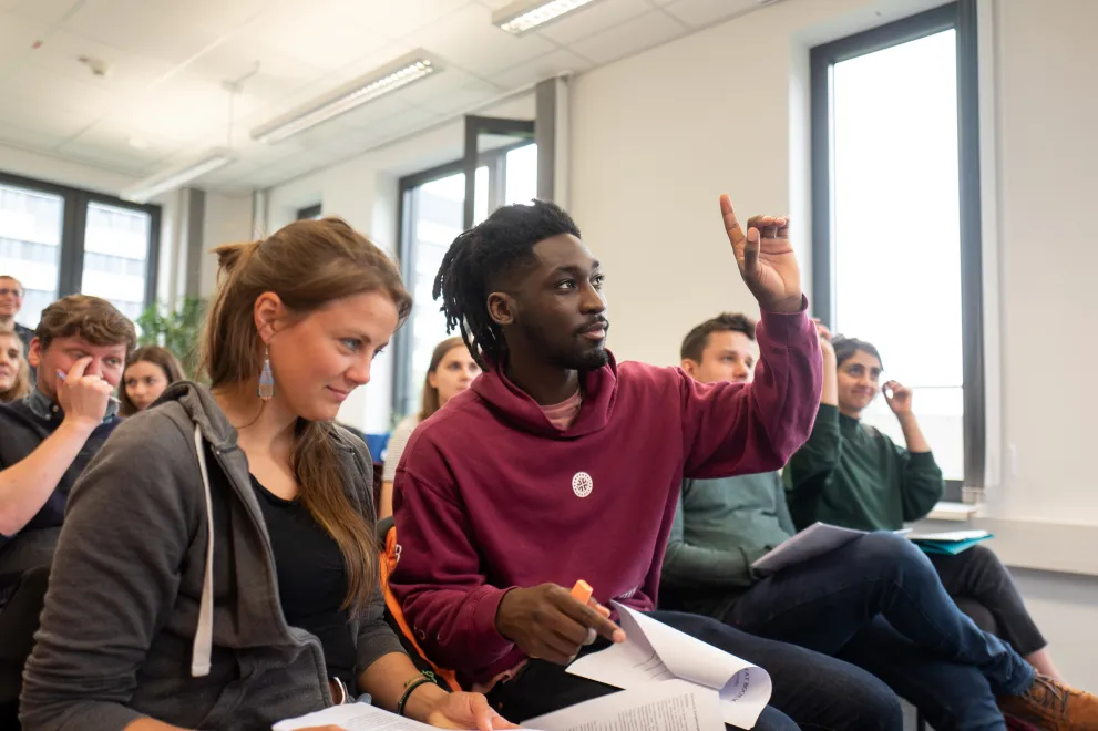  Student hebt die Hand bei einer Veranstaltung 
