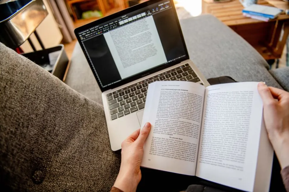 Person auf der Couch mit Buch und Laptop 