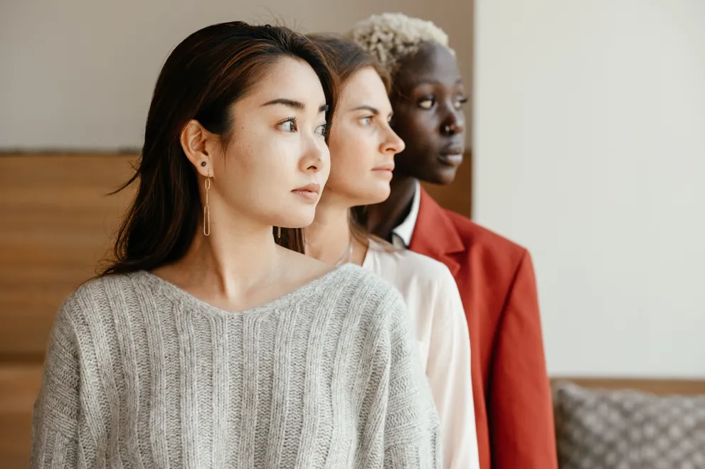 Drei Frauen verschiedener Ethnien schauen mit ernstem Gesichtsausdruck nach rechts.