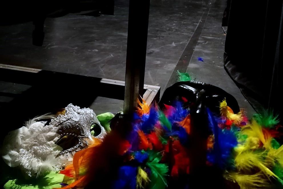 Masken, Federboas und weitere Kostümteile hinter Kulissen und Vorhang einer Theaterbühne