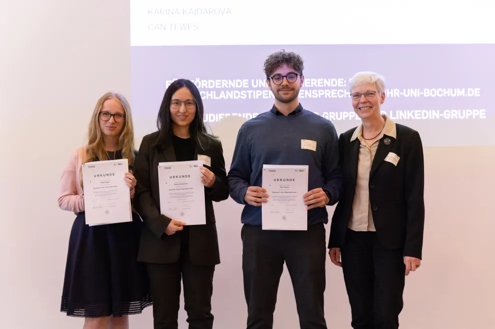 Foto: Vier Personen stehen nebeneinander und gucken in die Kamera. Drei Personen links halten alle jeweils eine Urkunde in den Händen.