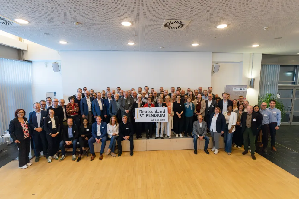 Foto: Personengruppe, in der Mitte halten Personen das Logo des Deutschlandstipendiums.