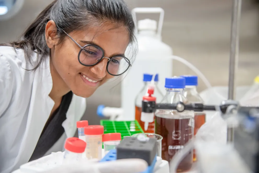 Eine junge Forscherin im Kittel mit Brille schaut auf eine Laborszenerie