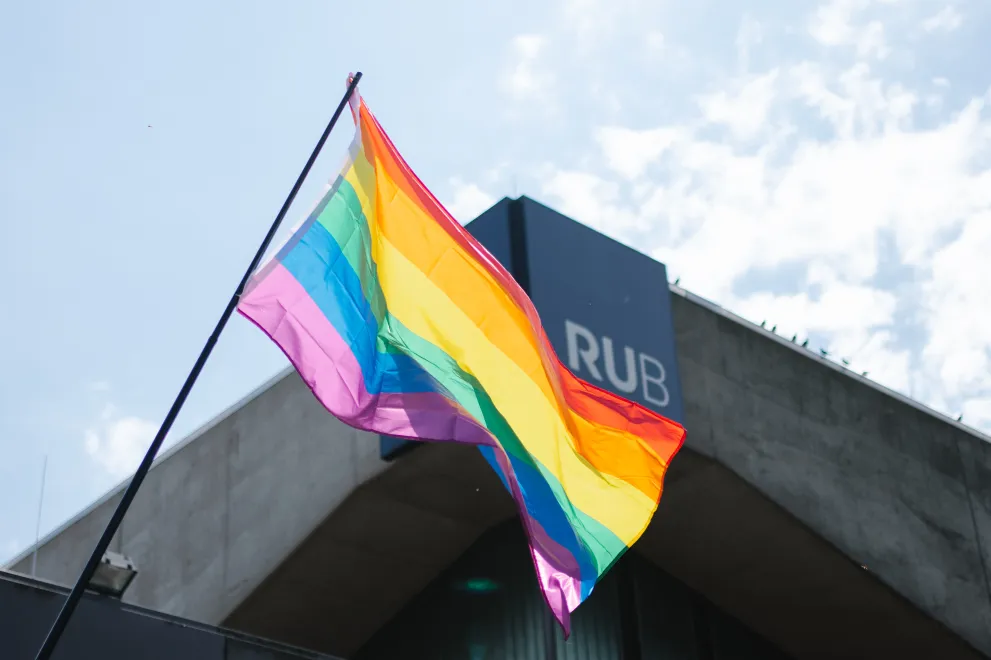 Eine Regenbogenflagge weht vor dem RUB-Schriftzug am Musischen Zentrum