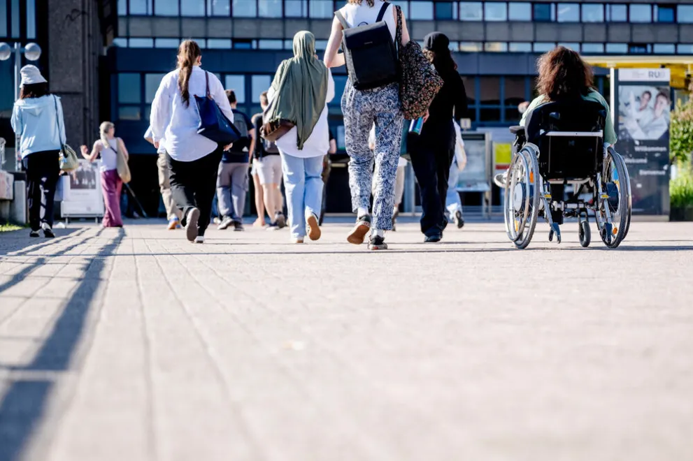 Unterschiedliche Menschen überqueren die Unibrücke, darunter eine Rollstuhlfahrerin und Personen mit Kopftuch