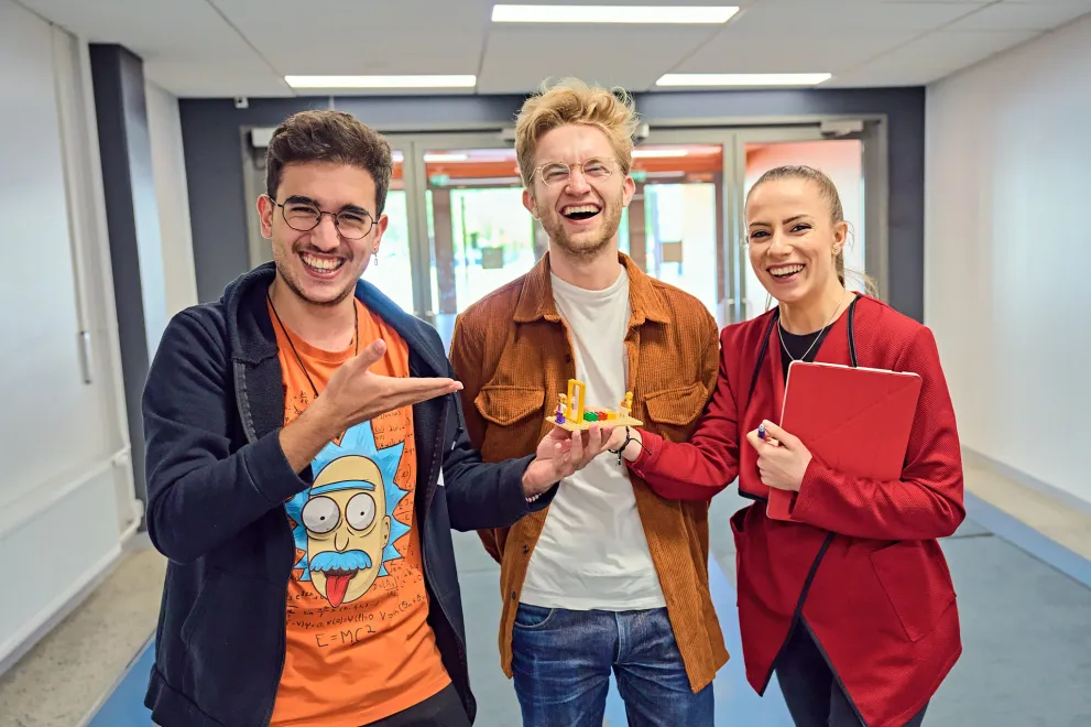 Foto: Drei lachende Studierende mit einem Lego-Modell
