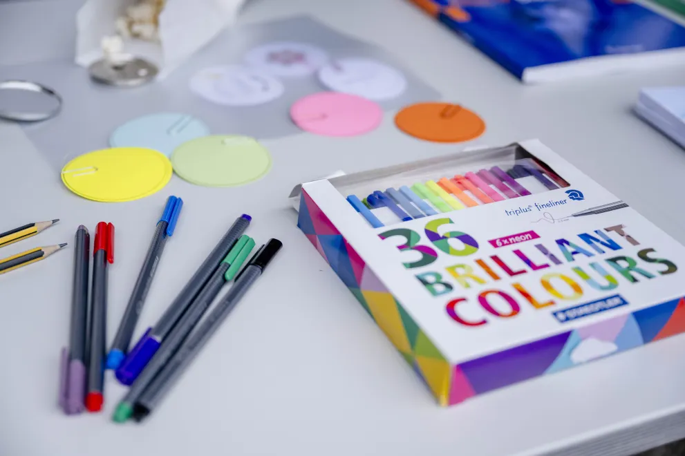 Bunte Stifte liegen auf einem Tisch. Auf der Packung steht „36 brilliant colours“ 