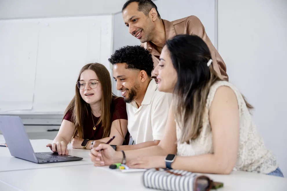 Foto: Vier Personen schauen gemeinsam auf einen Laptop. 