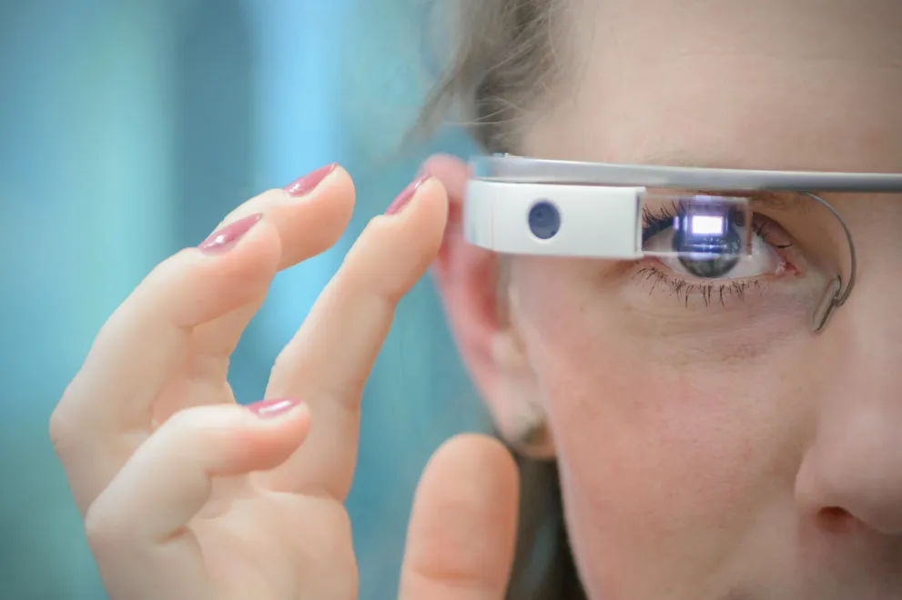 Foto: ein Teoi vom Gesicht einer Jungen Frau, die Smartglasses trägt uind eine Hand an den Sensor hält