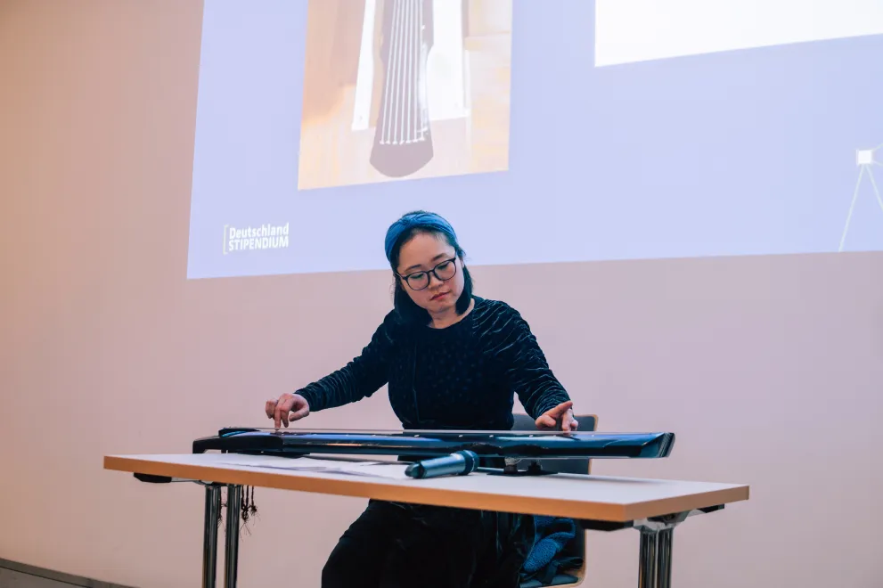 Foto: Eine Frau sitzt und spielt das chinesische Instrument Guqin, eine Griffbrettzither.