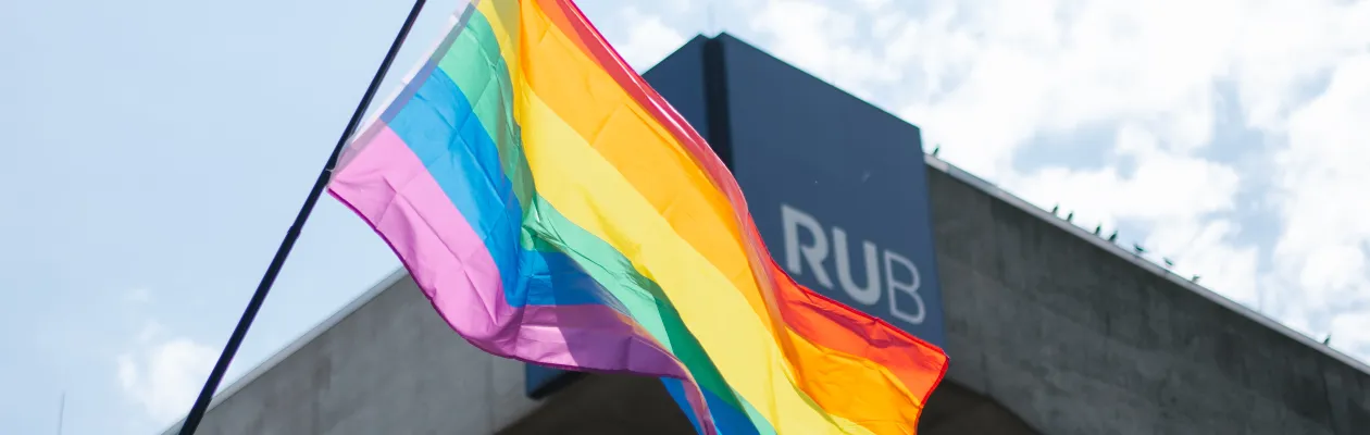 Eine Regenbogenflagge weht vor dem RUB-Schriftzug am Musischen Zentrum