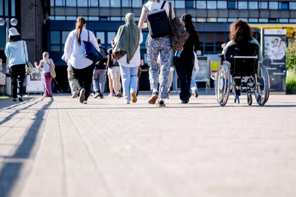 Unterschiedliche Menschen überqueren die Unibrücke, darunter eine Rollstuhlfahrerin und Personen mit Kopftuch