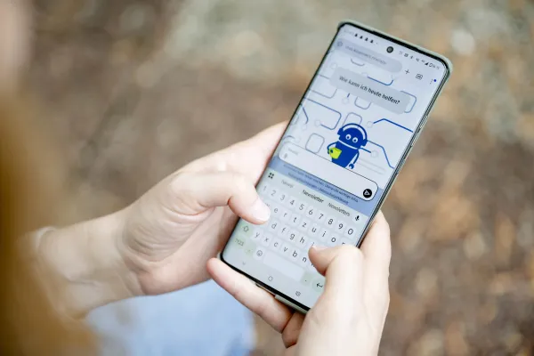 Das Foto zeigt ein Handy, das von einer Person gehalten wird, die auf der Oberfläche der Plattform KI:Connect etwas eintippt