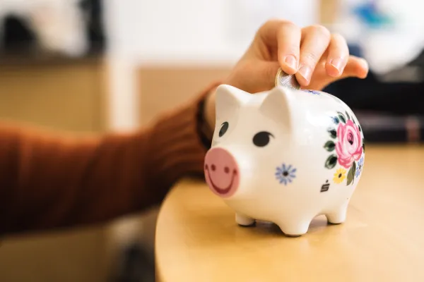 Foto: Sparschwein, in das jemand einen Euro legt.