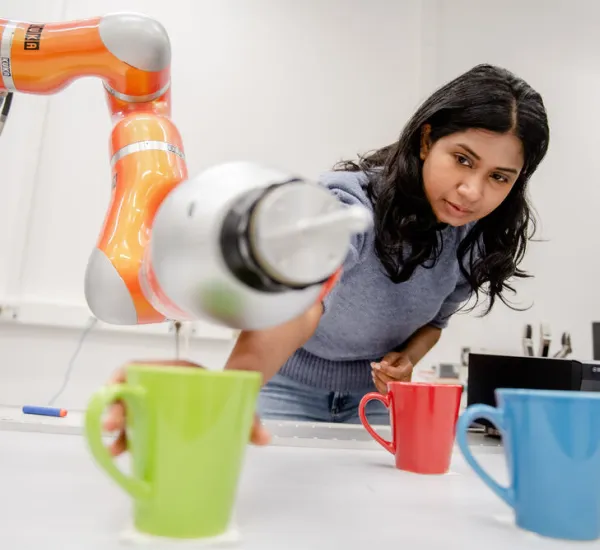 Eine Frau nimmt eine Tasse, in die ein Roboterarm Wasser schüttet